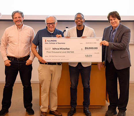 Ishva Minefee stands with ISOI leadership, receiving a large check symbolizing his Research Paper Prize.